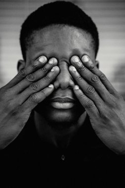 Genç, yakışıklı, Afro-Amerikan bir adamın portresi elleriyle gözlerini kapatıyor.