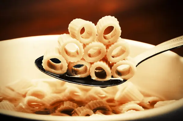 Närbild av en skål med makaroner soppa. Sked plocka upp makaroner, pasta. — Stockfoto