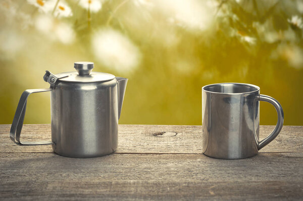 Tea time, stainless steel tea cup and teapot over wooden table outdoors