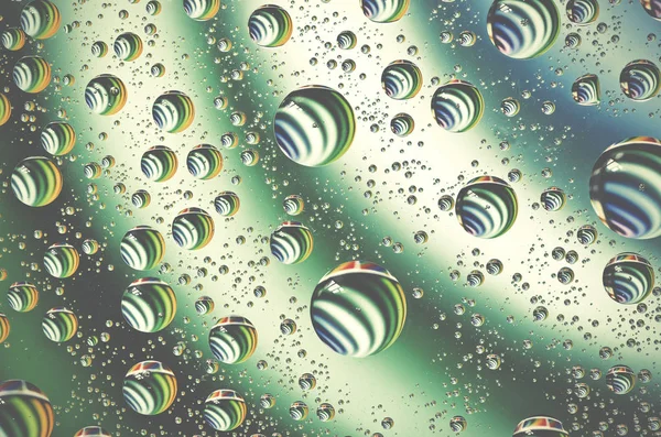 Água cai fundo na superfície verde. Gotas de água com reflexos neles . — Fotografia de Stock
