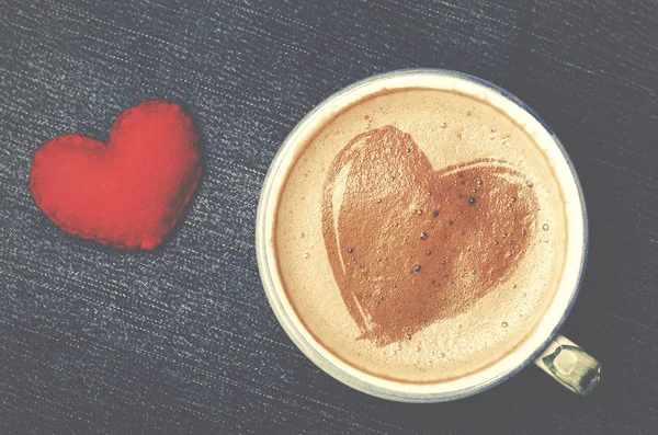 Kopje koffie met schuim in de vorm van hart op blue jeans, denim achtergrond cappuccino. Rood hart handgemaakte van vilt, dag van de Valentijnskaart concept. — Stockfoto