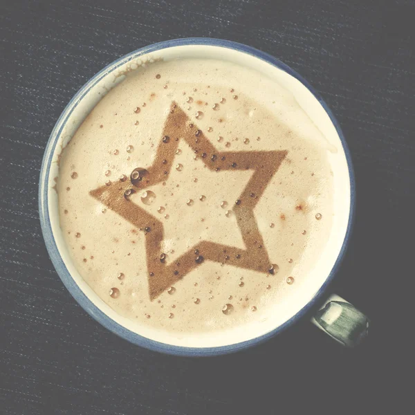 Чашка капучино кави з піною у вигляді зірки на блакитних джинсах, джинсовий фон. Біла дерев'яна зірка . — стокове фото