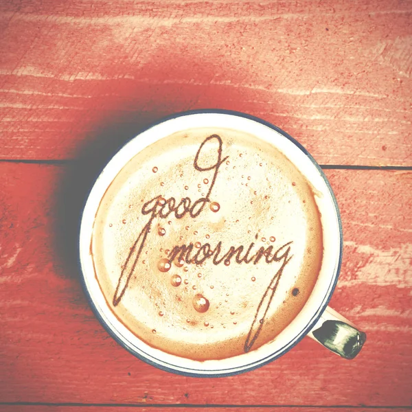 Una taza de café con leche, capuchino sobre una mesa de madera rosa. Palabras buenos días escritas en un café . —  Fotos de Stock