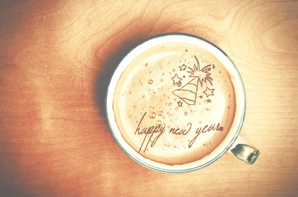 Φλιτζάνι καφέ στο ξύλινο τραπέζι καπουτσίνο. Ευτυχισμένο το νέο έτος λέξεις που σχηματίζονται από καφέ αφρός. — Φωτογραφία Αρχείου