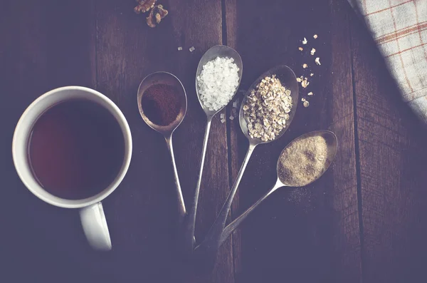 Ложки з цукром, кавою, вівсом та горіхами на справжньому коричневому дерев'яному столі. Чашка чаю . — стокове фото