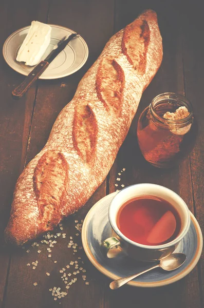 Homemade fresh baguette, plate with cheese, jar of natural honey and cup of tea on wooden table. — Stock Photo, Image