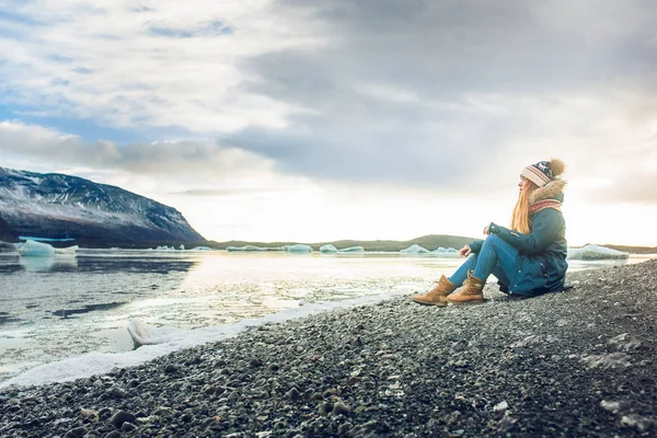 Woman sitting on seashore with black sand — Stock Photo, Image