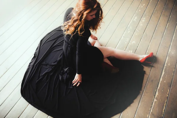 年轻美丽的红色头发妇女在地板上黑色礼服的肖像 — 图库照片