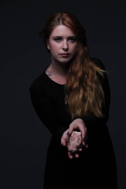Deniz taş koyu arka plan üzerinde tutarak siyah elbiseli genç güzel kızıl saçlı kadın portresi