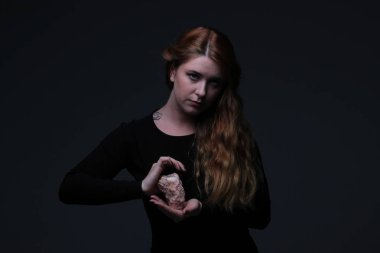 Deniz taş koyu arka plan üzerinde tutarak siyah elbiseli genç güzel kızıl saçlı kadın portresi