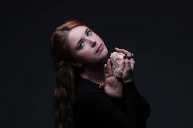 Deniz taş koyu arka plan üzerinde tutarak siyah elbiseli güzel kızıl saçlı kadın portresi