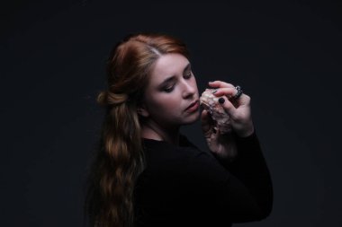 Deniz taş koyu arka plan üzerinde tutarak siyah elbiseli güzel kızıl saçlı kadın portresi