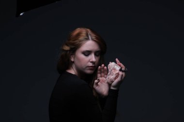 Deniz taş koyu arka plan üzerinde tutarak siyah elbiseli genç güzel kızıl saçlı kadın