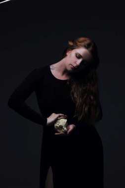 Deniz taş koyu arka plan üzerinde tutarak siyah elbiseli genç güzel kızıl saçlı kadın portresi