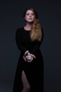 Deniz taş koyu arka plan üzerinde tutarak siyah elbiseli genç güzel kızıl saçlı kadın portresi