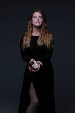 Deniz taş koyu arka plan üzerinde tutarak siyah elbiseli genç güzel kızıl saçlı kadın portresi