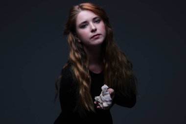 Deniz taş koyu arka plan üzerinde tutarak siyah elbiseli genç güzel kızıl saçlı kadın portresi