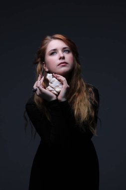 Deniz taş koyu arka plan üzerinde tutarak siyah elbiseli genç güzel kızıl saçlı kadın portresi