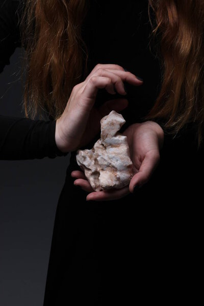 close-up of woman in black dress holding beautiful sea stone in hands on dark background