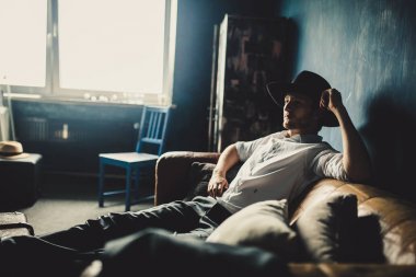 pencere arka plan, kahverengi kanepede oturan şapkalı yakışıklı düşünceli adam portresi