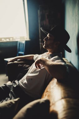 Oda arka plan, kahverengi kanepede oturan şapkalı yakışıklı düşünceli adam portresi