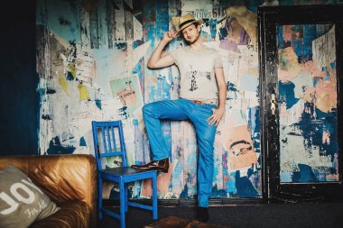 Oda arka plan, kahverengi kanepe yakınındaki şapkalı genç yakışıklı adam portresi