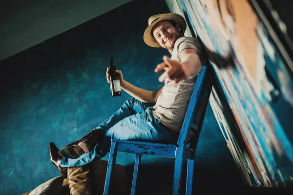 Retrato Joven Guapo Hombre Sombrero Sosteniendo Botella Sentado Silla Azul — Foto de Stock