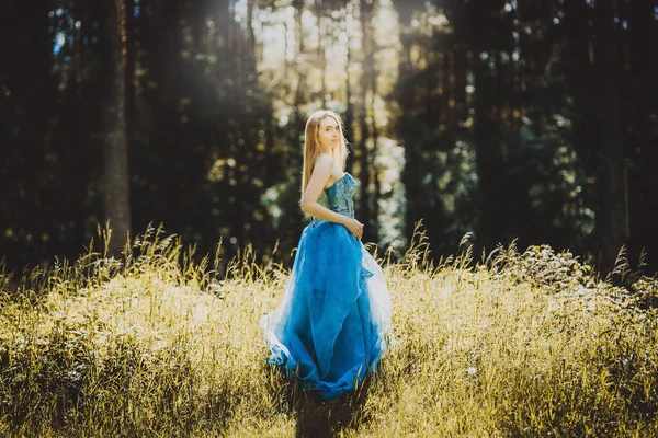 full length of young blonde woman with long hair and blue dress on forest background