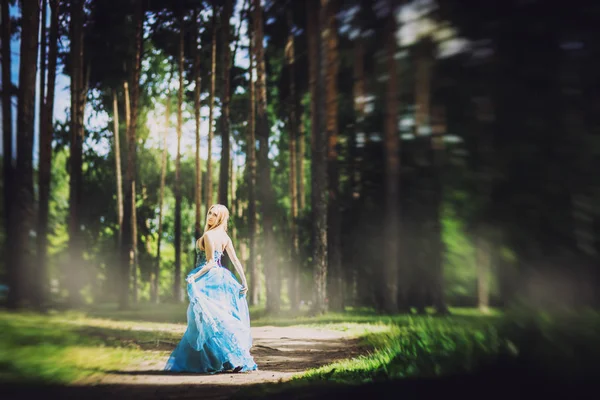 full length of young blonde woman with long hair and blue dress on forest background