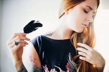 Genç Moda kadın portresi gözler kapalı, Kızıl saçlı ve siyah saten siyah karga tüy tutan oda duvar arka plan üzerinde elbise