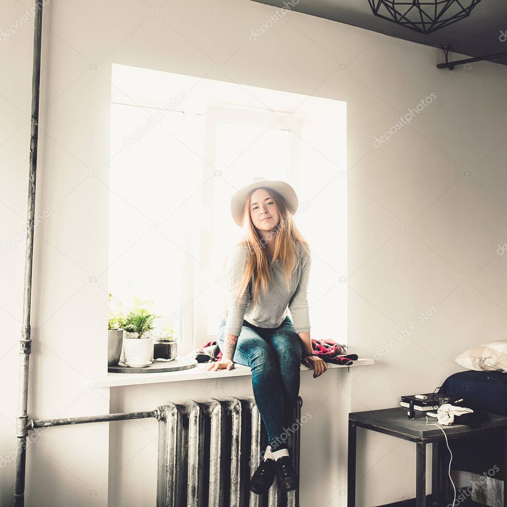 young fashion woman with red hair in hat sitting on windowsill on window background