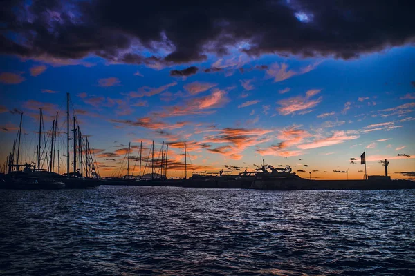 photo of beautiful seascape with boats silhouette on sea and rainy clouds in sky at sunset