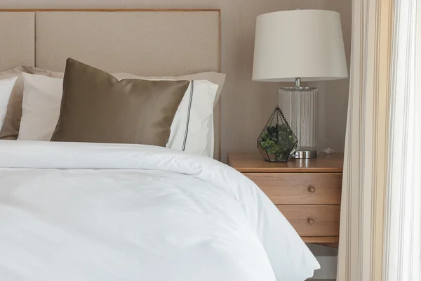 Brązowy poduszkę na białe nowoczesne łóżko z lampka na stolik — Zdjęcie stockowe