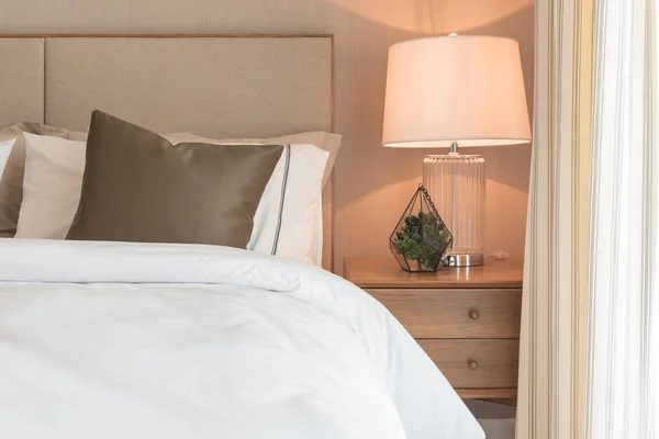 Brown pillow on white modern bed with lamp on table side — Stock Photo, Image