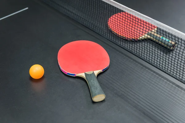 Raquette de ping-pong avec balle orange sur fond noir — Photo