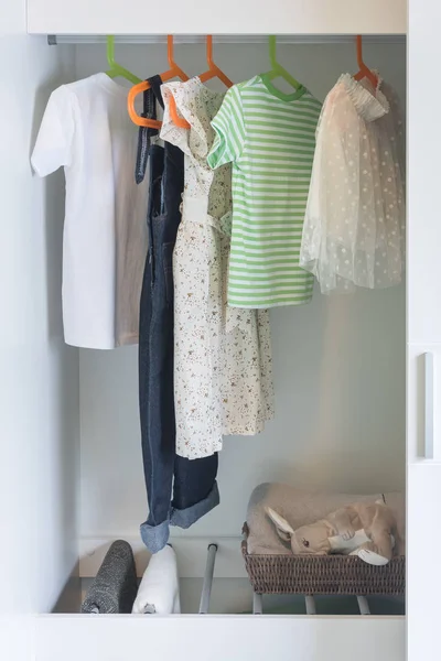 Kid's clothes hanging on rails in wooden wardrobe — Stock Photo, Image