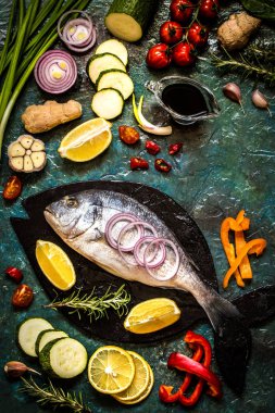 Sebzeler, limon, baharat ve yeşillik üzerinde mavi bir arka plan ile Dorada balık
