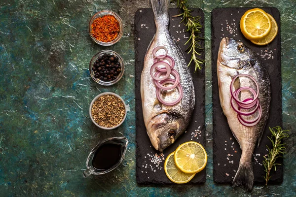 Sebzeler, limon, baharat ve yeşillik üzerinde mavi bir arka plan ile Dorada balık