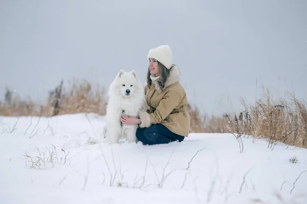 Młoda dziewczyna spaceruje zimą z białym Żabim psem na zaśnieżonej łące w lesie. — Zdjęcie stockowe