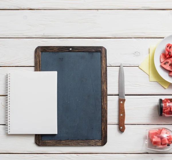 Svarta tavlan och anteckningsbok på ett skrivbord med vattenmelon. — Stockfoto