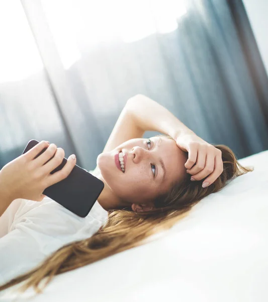 Ragazza adolescente che sogna in un letto con uno smartphone . — Foto Stock