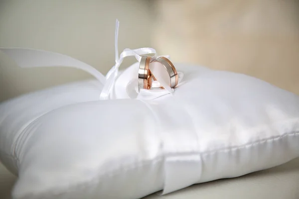 White and red gold wedding rings on a white satin cushion — Stock Photo, Image