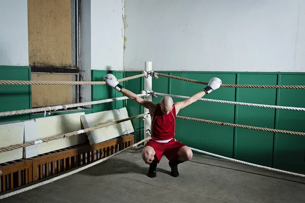 Joven adulto macho boxeador en rojo ropa squat y mantener el lado cuerdas — Foto de Stock