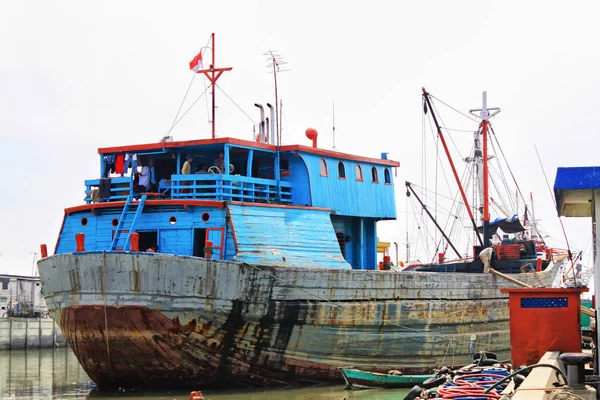 Colorful rusty phinisi ship in Jakarta harbor with fishermen on