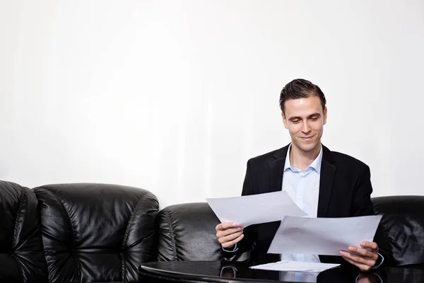 Male adult business man in a suit sitting on a sofa, looking at paperwork — Stock Photo, Image
