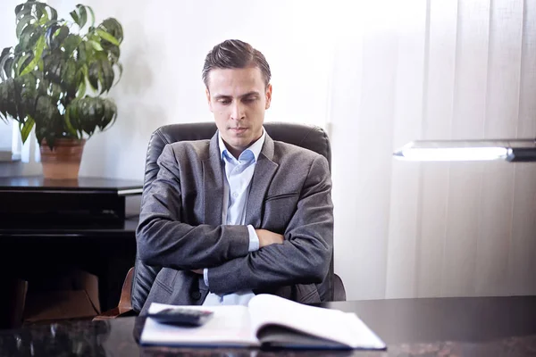 Hombre adulto en un traje sentado en una silla detrás del escritorio en un —  Fotos de Stock