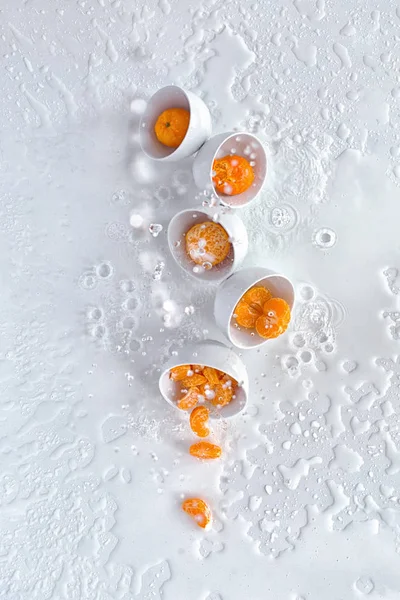 Пять белых чаш с мандаринами, брызги воды, белый фон, вид сверху Лицензионные Стоковые Изображения