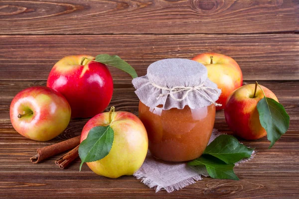Glass jar of homemade apple jam with fresh fruits and ingredients on woody background