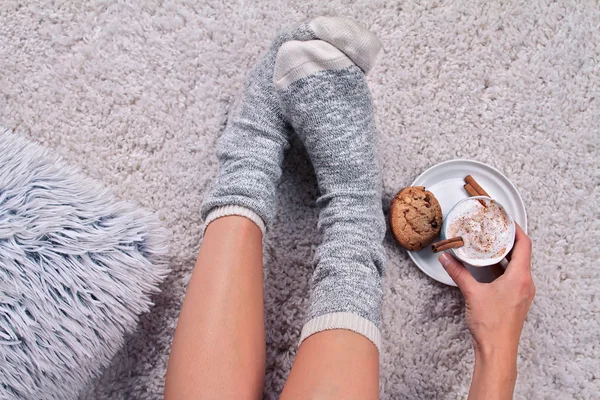 Woman wearing cozy warm wool socks relaxing at home, drinking cacao, winter lazy day concept, top view. Soft, comfy lifestyle.