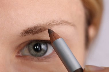 Young beautiful woman applying eyebrow pencil close up. Beauty, make up concept clipart